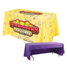 The image shows two tables covered with cloths. The top table has a yellow cloth with popcorn and FREDDIES POPCORN COMPANY in red and white text. The bottom table has a plain purple cloth.