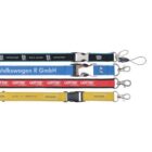 Four lanyards are displayed side by side, each with different colors and text. From top to bottom: a black one, a green and blue one, a red one, and a yellow one, each with a metal clip and a plastic buckle.