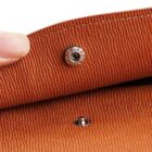 Close-up of a person holding open a brown textured leather wallet flap, revealing a small metal snap button.