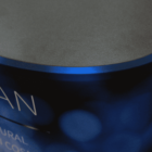 A close-up of a blue and black cylindrical object with partially visible white text. The top surface appears smooth and metallic. The focus and lighting create a blurred effect on some parts of the image.