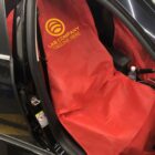 Car seat covered with a red protective sheet featuring a yellow logo and text LAB COMPANY TAGLINE HERE. A small bottle and a gear stick are visible in the cars interior.