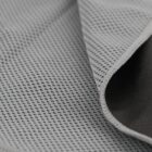 Close-up of a textured, gray fabric with small perforations, showing the edge folded back to reveal a darker underside. The material appears flexible and breathable, suitable for activewear or sports clothing.