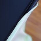 A close-up of a light green fabric edge tucked under a black surface, possibly a table. The background shows a wooden floor.