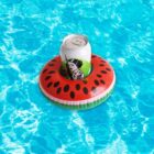 A soda can with a retro-style illustration floats in a small inflatable ring shaped like a watermelon slice, set against a bright blue swimming pool background.