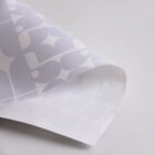 Close-up of a sheet of semi-transparent patterned paper, with geometric shapes and soft curves, on a white surface. The edges of the paper are slightly curled.