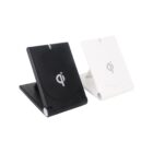 Two foldable wireless chargers, one black and one white, stand side by side. Both have the Qi logo on the front and are set on a white background.