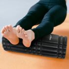 Person using a foam roller under their legs while lying on a yoga mat.