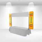 A white exhibition booth with a long table covered in a white cloth. Two vertical yellow banners on each side display COMBO Deals and TODAY in bold letters. The setup is in a white room with spotlights above.