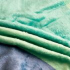 Close-up of layered fabric in various shades: light green, mint green, turquoise, and light blue. The textures appear soft and plush, like velvet or suede.