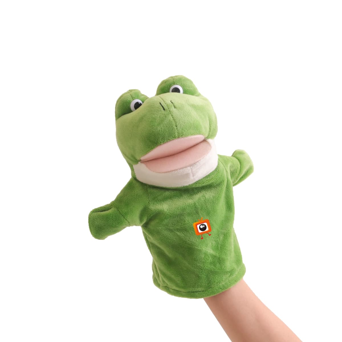 A plush frog puppet with expressive eyes and a wide-open mouth is on a persons hand. The puppet is green with a lighter face and features a small, embroidered orange square with a black and white circle on its chest.
