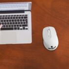 Laptop and wireless mouse on a wooden desk, with a hand typing on the keyboard.