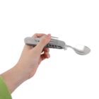 A hand is holding a multifunctional utensil that combines a fork and spoon, with other tools folded inside. The background is plain white.