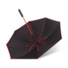 A black umbrella turned upside down, showing its red ribs and handle. The umbrella is open and resting on a white surface.