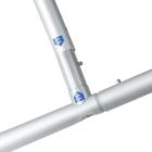 Close-up of a metallic frame joint, composed of cylindrical rods connected by tube clamps. The metal has a matte finish and features small arrow symbols on the frames. The framing forms an angle, showcasing its structural design.