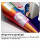 Close-up of colorful satin fabric with a silver-coated finish. Another inset image shows a hand holding a roll of the same silver fabric. Text states: 160g Silver Coated Satin. Premium material with quality assurance. Good quality and perfect for durable use.