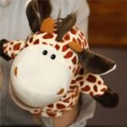 A plush giraffe hand puppet with brown spots and a friendly expression is being held. Its ears, mane, and tail are fuzzy, adding a playful touch to its design. The background is blurred.