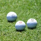 Three white golf balls with different logos are placed on green grass. Each ball has a unique design and the word Lorem beneath the logo.