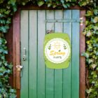 A green door surrounded by lush ivy features a Spring Party sign with decorative leaves and a sun graphic. A rusted lock and handle are visible on the door.