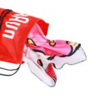 Red drawstring bag with a white text logo containing a colorful, cartoon-themed towel peeking out. The towel features pink, red, and white designs with black outlines.