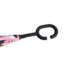 Close-up of an umbrella handle shaped like a wide, flat letter C in black. The umbrella fabric is partially visible, showing pink and black patterns.