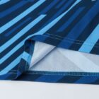 Close-up of a blue garment with a geometric pattern featuring various shades of blue stripes. The edge of the fabric is visible, highlighting the stitching and the folded hem.