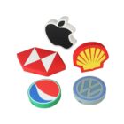 Five USB drives in shapes of various logos: a black apple, red and white geometric design, yellow shell with red border, red, white, and blue circle, and a blue circle with a white VW initials.