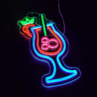 Neon sign depicting a tropical cocktail glass with a straw and bubbles, outlined in blue and filled in red. A green and red garnishment resembling a cherry or fruit decorates the rim. The sign is set against a black background.