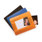 Stack of three colored sheets: black, blue, and orange. The orange sheet features text and a rectangular cutout revealing a photo beneath it. Visible in the photo are two people smiling.