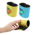 Hand holding a yellow neoprene wristband with a colorful tropical logo. Two more wristbands are shown above, one yellow and one blue, both with the same logo. The wristbands appear flexible and designed for grip support.