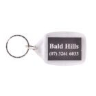 A transparent keychain with a metal ring features a black insert. The insert displays the text Bald Hills (07) 3261 6033 in white lettering.
