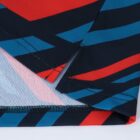 Close-up of a folded fabric corner with a zigzag pattern in red, blue, and black. The fabric shows stitching details and a small slit at the edge, highlighting the colorful, geometric design.