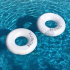 Two white pool floats in a clear blue swimming pool. One float is labeled BRUNETTE and the other BLONDE. They are close together, creating a fun contrast against the water.