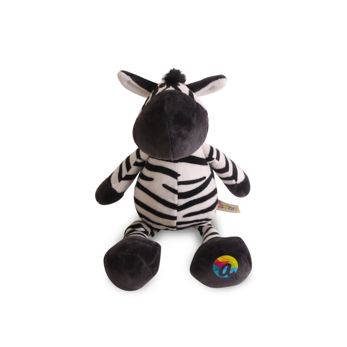Stuffed toy zebra with black and white stripes, large ears, and a playful expression. Its right foot features a colorful emblem. The toy is seated on a plain white background.