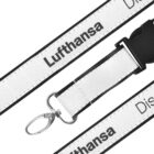 A close-up of a white and black lanyard with the word Lufthansa printed on it in black. The lanyard has a metal hook and a plastic buckle clasp, designed for holding badges or keys.