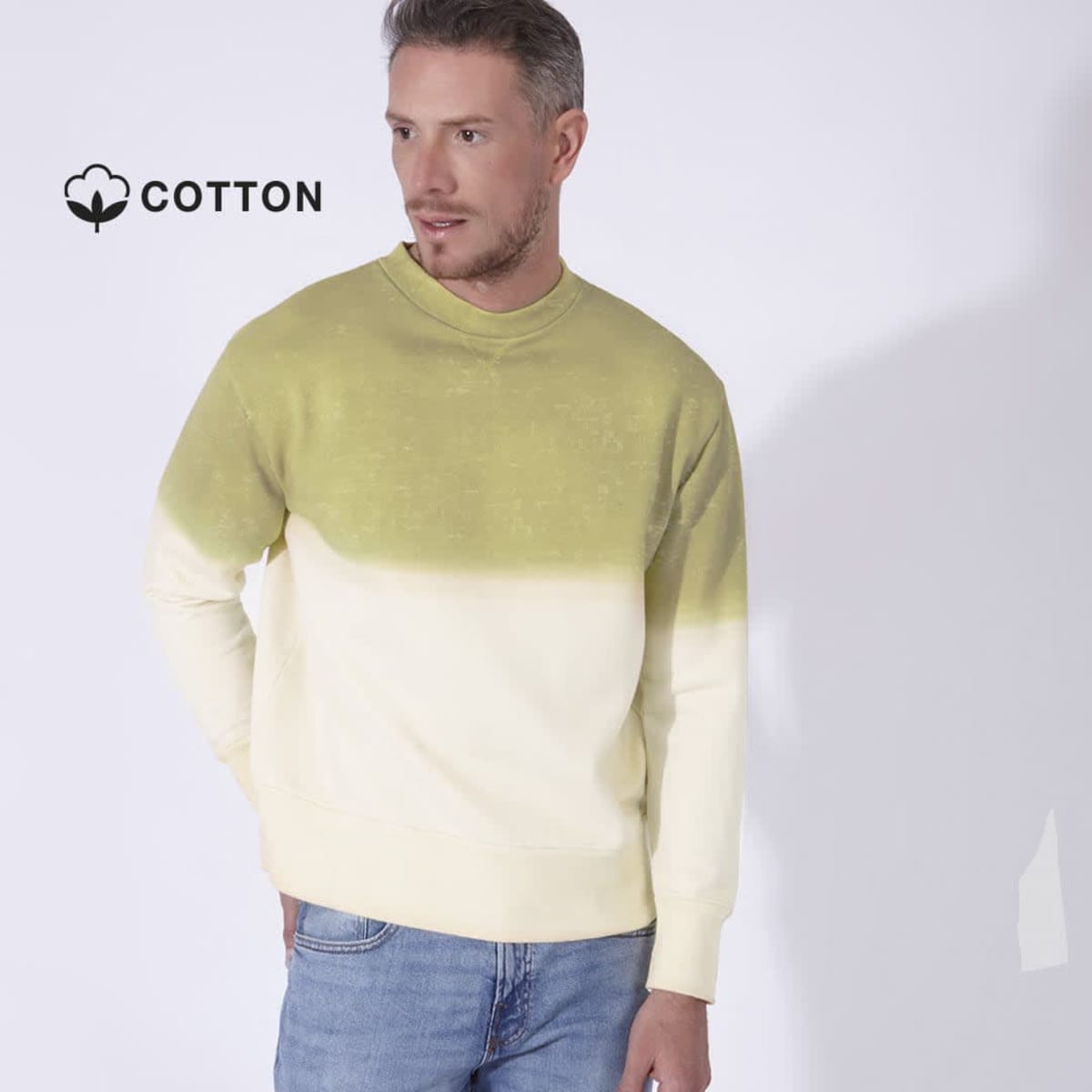 Man wearing a two-toned green and cream sweatshirt with blue jeans. He has a neutral expression and is standing against a plain background. A cotton icon is visible at the top left, indicating the material of the clothing.
