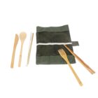 Reusable bamboo cutlery set with a knife, spoon, chopsticks, fork, and a metal straw. The set is placed next to a green canvas pouch with a button closure. The utensils are made of natural bamboo.
