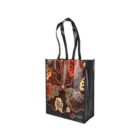 A tote bag with black handles features an Indigenous Australian art design with earthy tones like brown, orange, and black. It includes organic shapes and patterns reminiscent of traditional Aboriginal artwork.