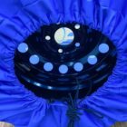 A close-up of a tire wrapped in a blue protective cover with gathered edges. Visible is a black metal wheel rim with circular holes. A cord is attached, hanging over the cover.