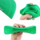Close-up images of a flexible, green silicone object being squeezed and bent by a hand. The material appears soft and pliable. The brand name is partially visible on the top left corner.
