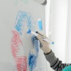 Person drawing red and blue recycle symbol on whiteboard with blue marker.