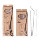 Two boxes of stainless steel drinking straws. Each box displays an illustration of a lemon and glass with a straw. In front of the boxes are two metal straws, one straight and one bent, accompanied by a cleaning brush.
