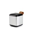 A compact, silver cube-shaped portable speaker with a black top featuring small holes for sound. A leather strap is attached for easy carrying. The design is sleek and minimalist.