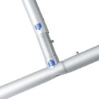 Close-up of a metallic joint connecting three silver poles, with blue labels featuring arrows on each segment. The joint appears to be part of a structural frame.