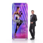 A poster displays a woman in athletic attire running with the text WILL IS POWER. A man in a suit stands beside the poster, posing. The background features vibrant purple lighting.