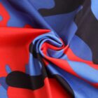 A close-up of fabric twisted into a swirl, featuring a vibrant camouflage pattern in red, blue, and black colors. The fabrics texture is smooth and glossy.