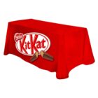 A rectangular table covered with a red cloth featuring the Kit Kat logo. The logo includes the text Kit Kat in white letters within an oval, with two chocolate-covered wafers underneath.