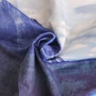 A close-up of a folded fabric with a smooth texture, featuring a blend of blue, purple, and white colors. The material appears soft, with a gentle swirl pattern created by the folds.