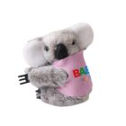 Stuffed koala toy wearing a pink bib with multicolored letters. The koala is gray with a black nose and white ears, holding a black plastic fork in its paw.