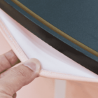 A close-up of a hand holding the edge of a black, spiral-bound notebook with a visible pink and white layered fabric or material underneath. The focus is on the texture and layers.