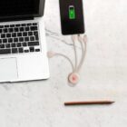 A laptop, a charging phone showing a full battery icon, a multi-connector charging cable, and a pencil are on a marble surface.